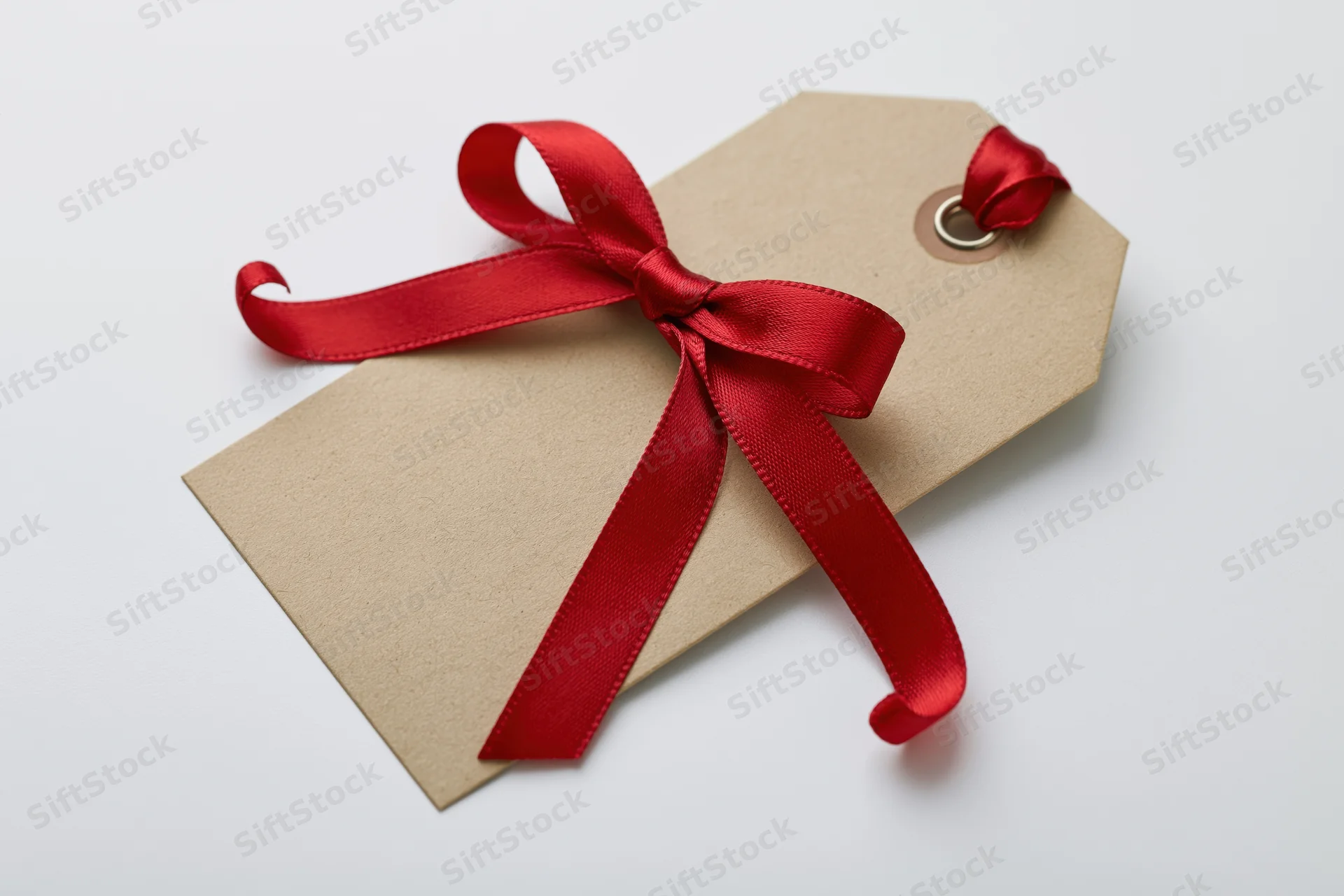 Blank kraft paper gift tag with red satin ribbon bow on white background