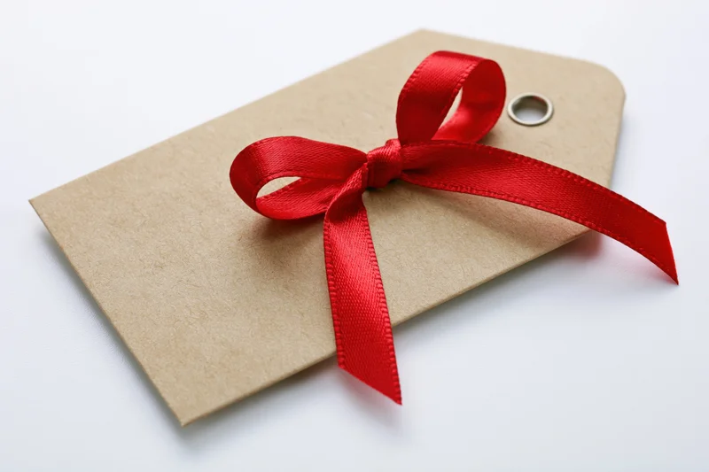 Blank kraft paper gift tag tied with a red satin ribbon bow on white background
