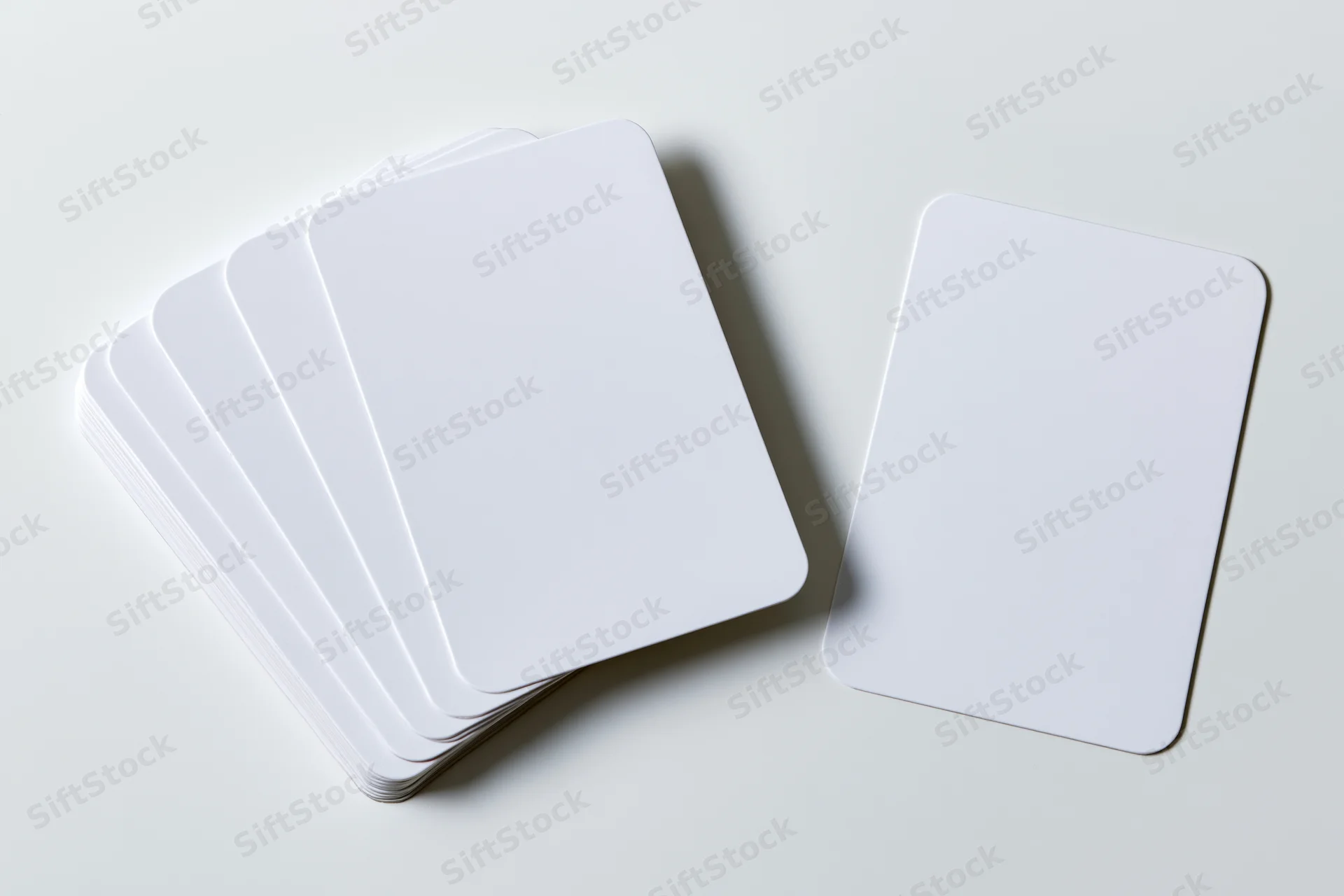 Blank white cards with rounded corners arranged in a stack and one separate on a plain surface