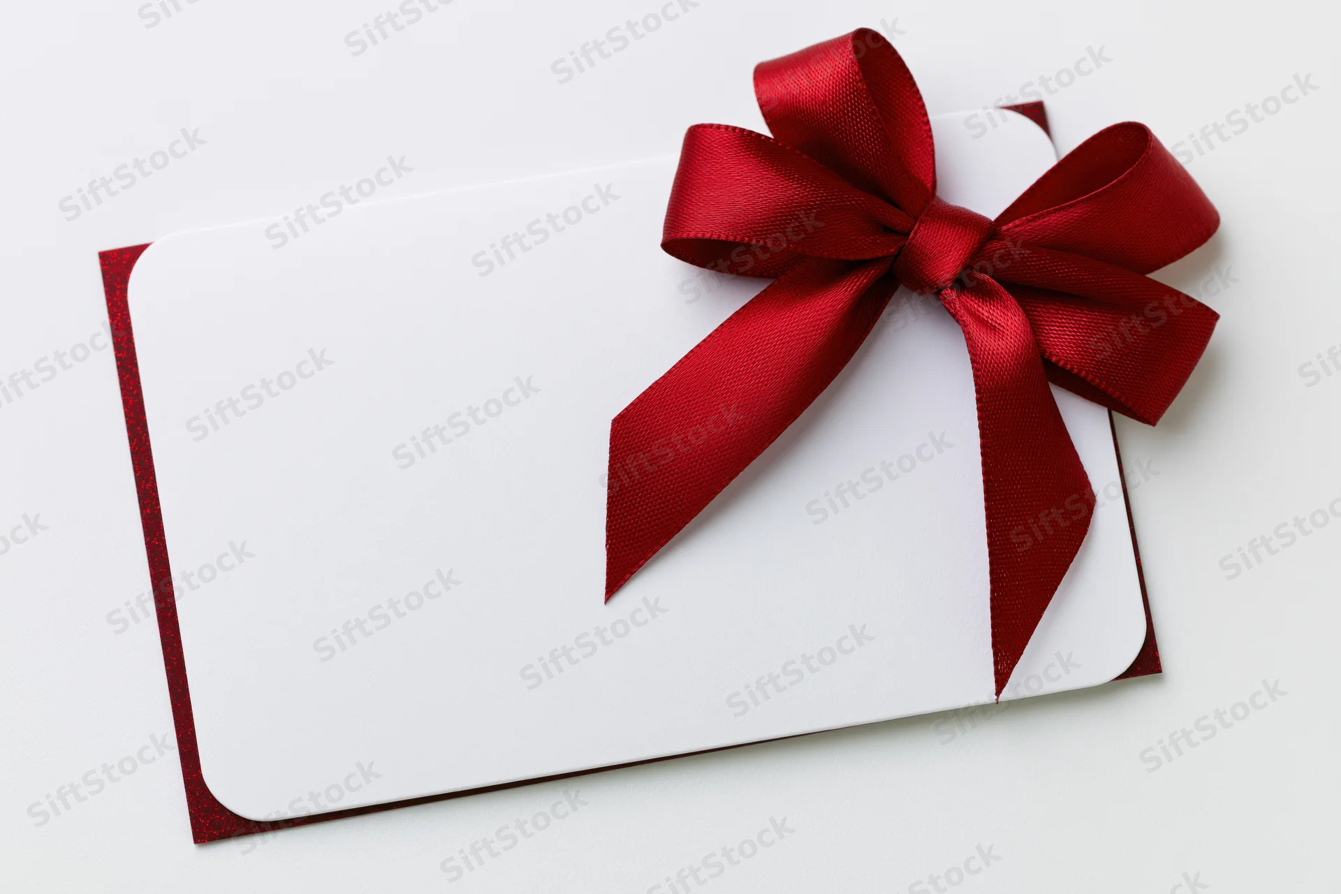 Blank white gift card with red satin ribbon bow on white background