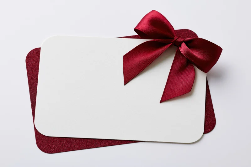 Blank white gift card with red satin ribbon bow on white background