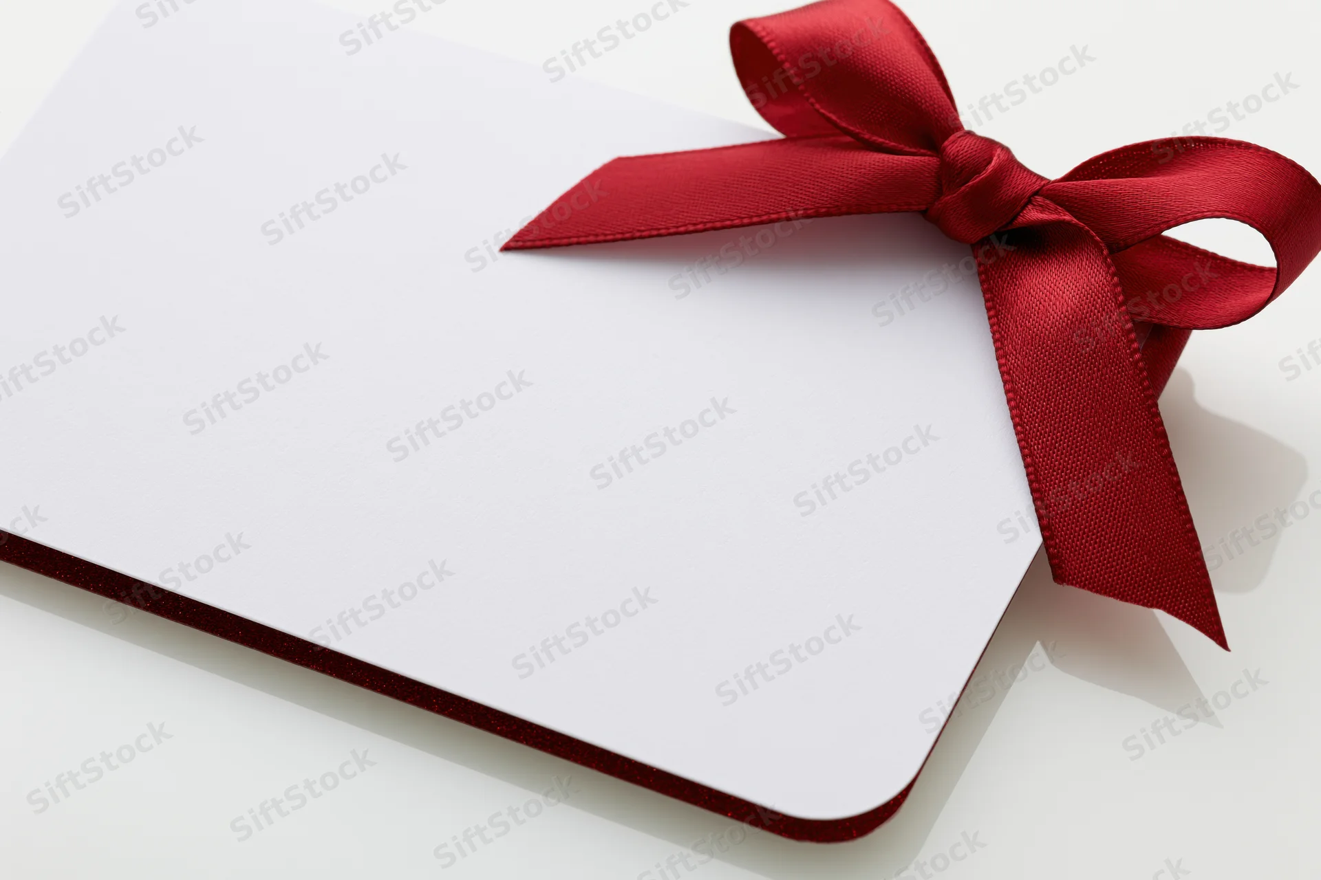Blank white gift card with red satin ribbon bow on white surface