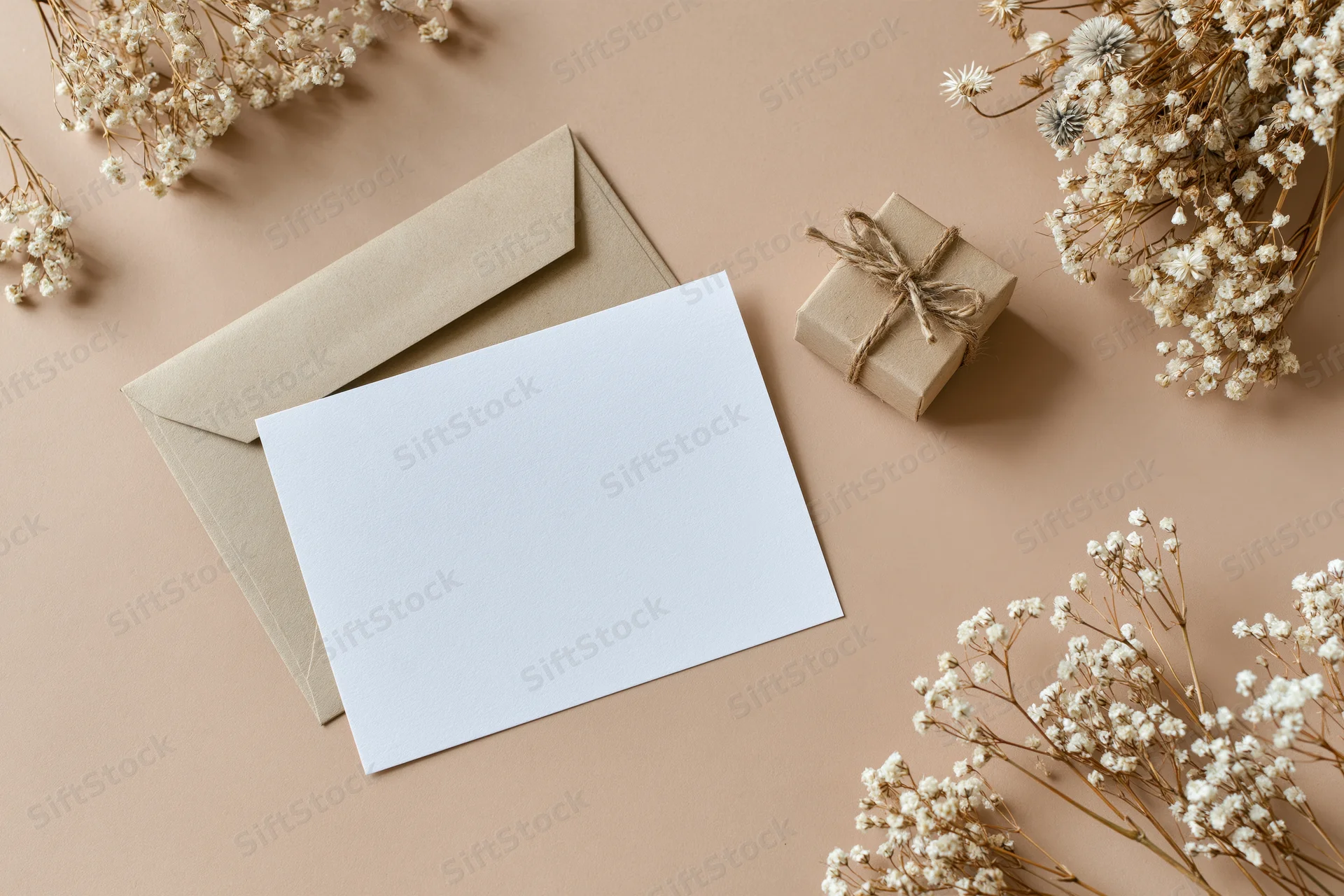 Blank white card with kraft envelope and dried flowers arranged on beige surface