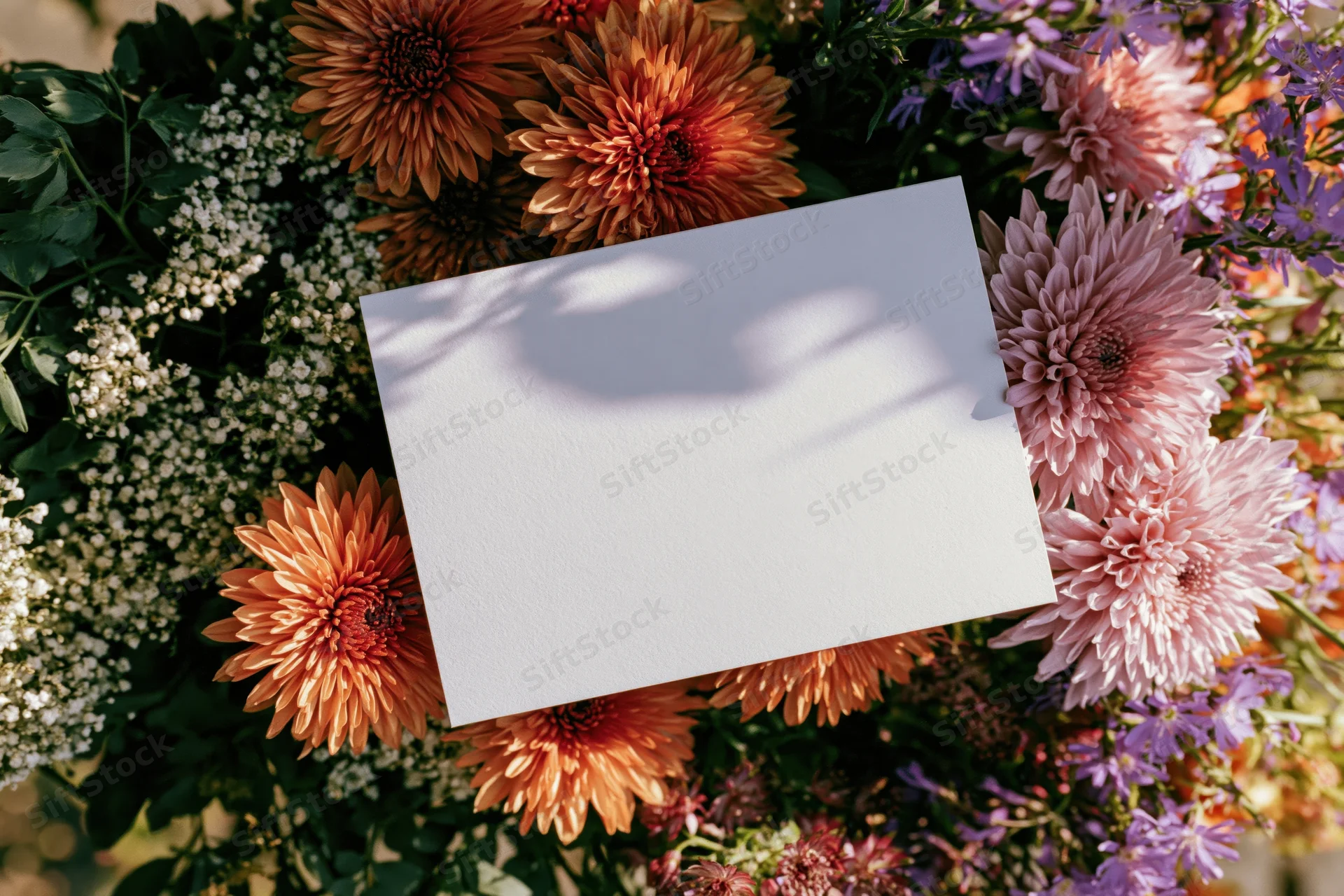 Blank white card resting on a colorful floral bouquet with dahlia, aster, and baby's-breath flowers