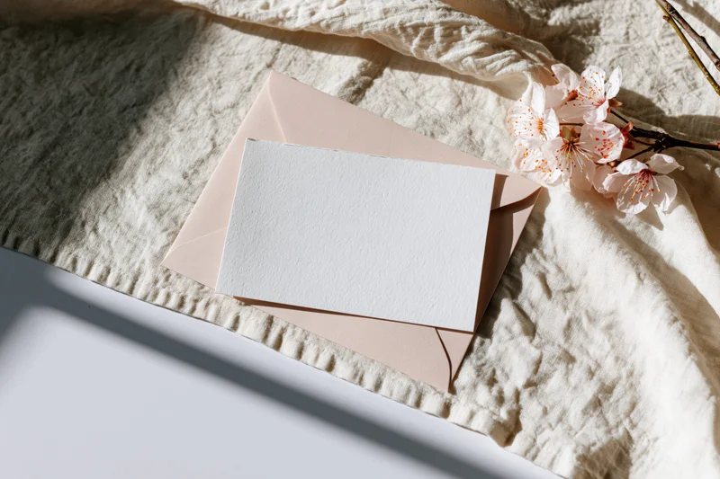 Blank textured card on blush envelope with cherry blossoms on linen fabric