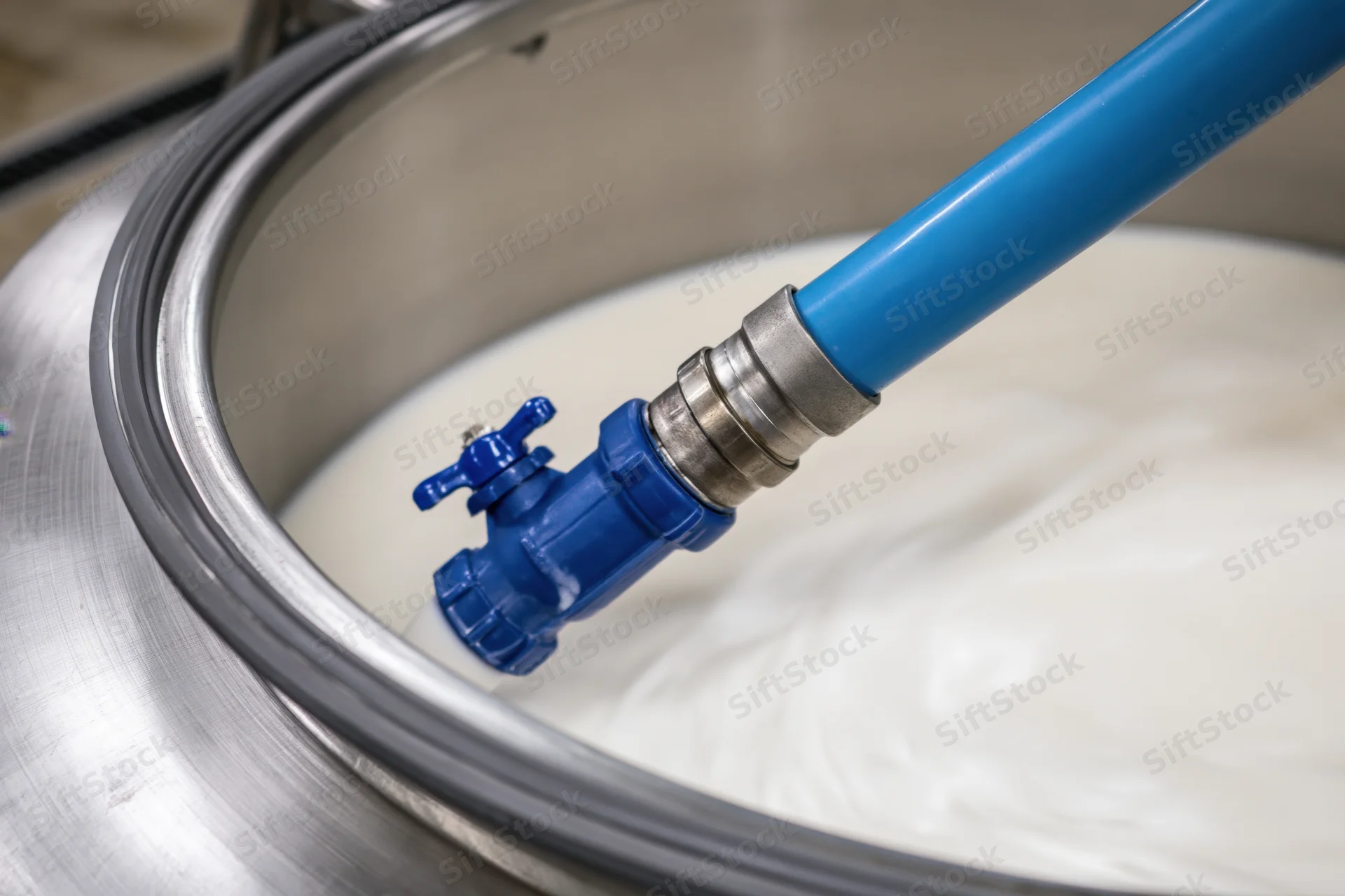 Blue hose pumping milk into stainless steel tank in dairy processing facility