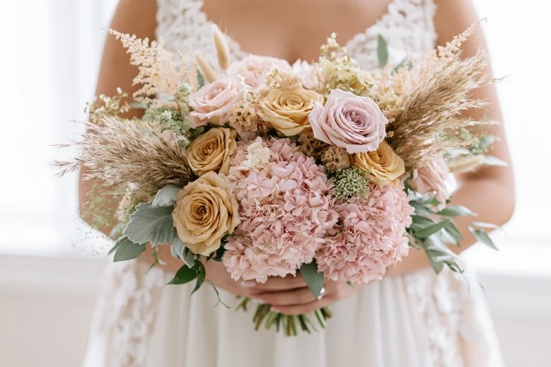 Bride holding a large floral bouquet in front of her body, wearing a white lace wedding dress