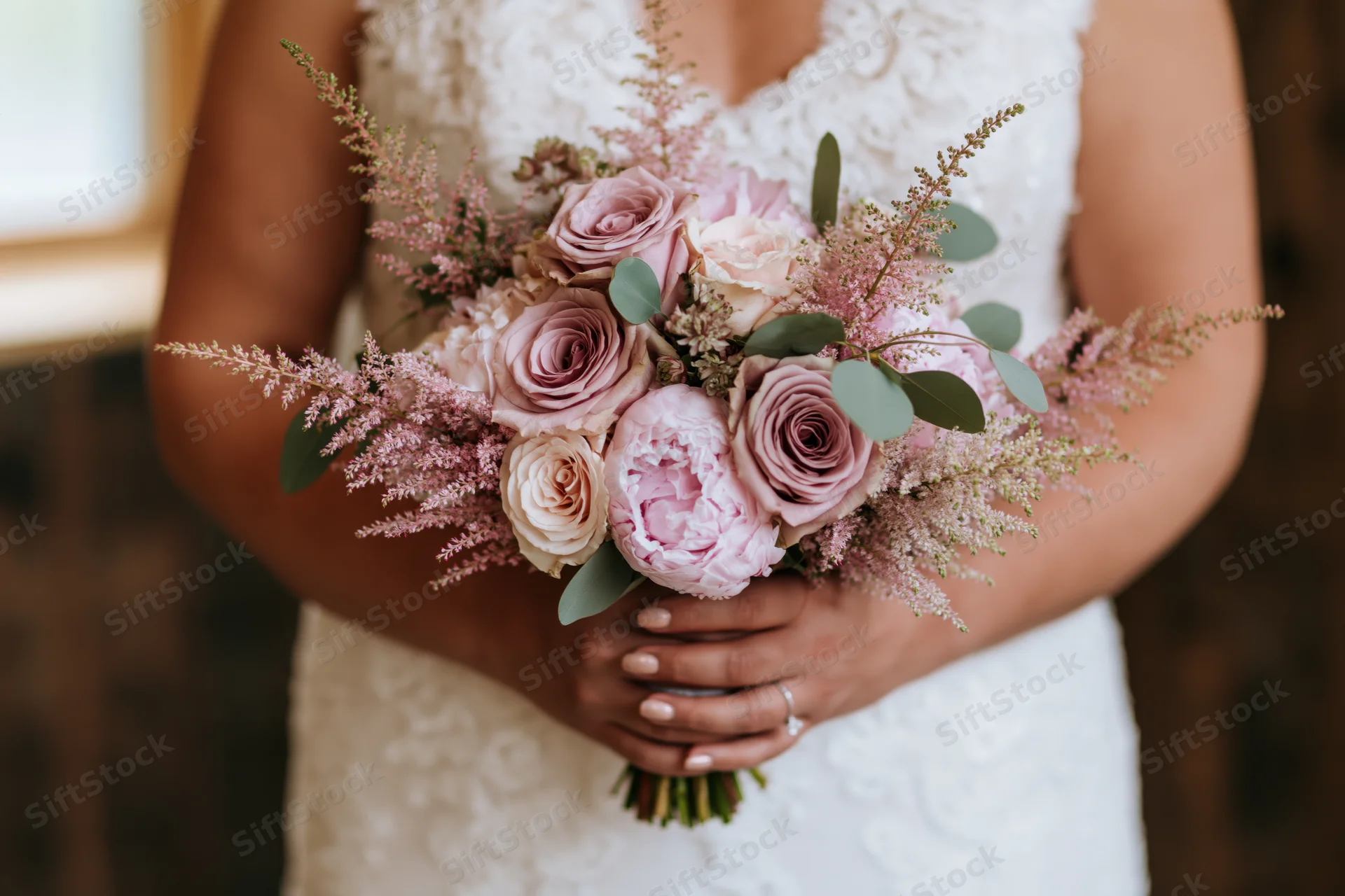Bride holding a bouquet of dusty mauve roses and blush peonies with astilbe and greenery in a lace wedding dress