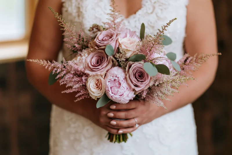 Bride holding a bouquet of dusty mauve roses and blush peonies with astilbe and greenery in a lace wedding dress