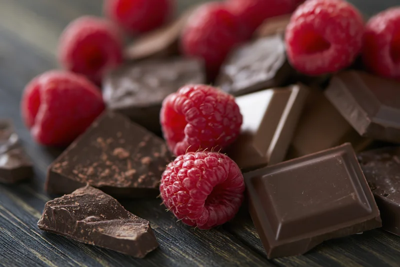 Broken dark and milk chocolate pieces with fresh raspberries on a dark wooden surface