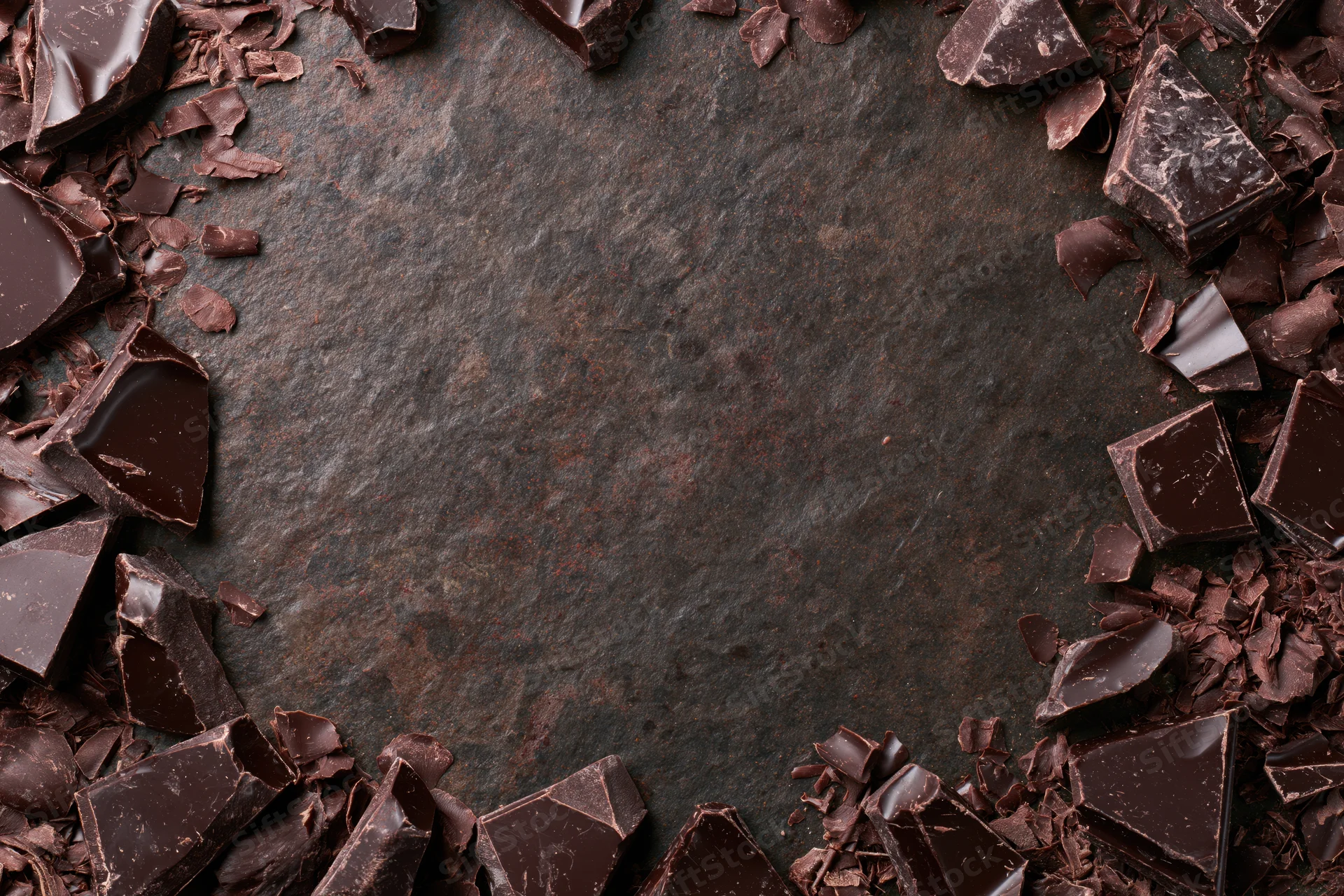 Broken dark chocolate chunks and shavings arranged in a frame around a dark stone surface