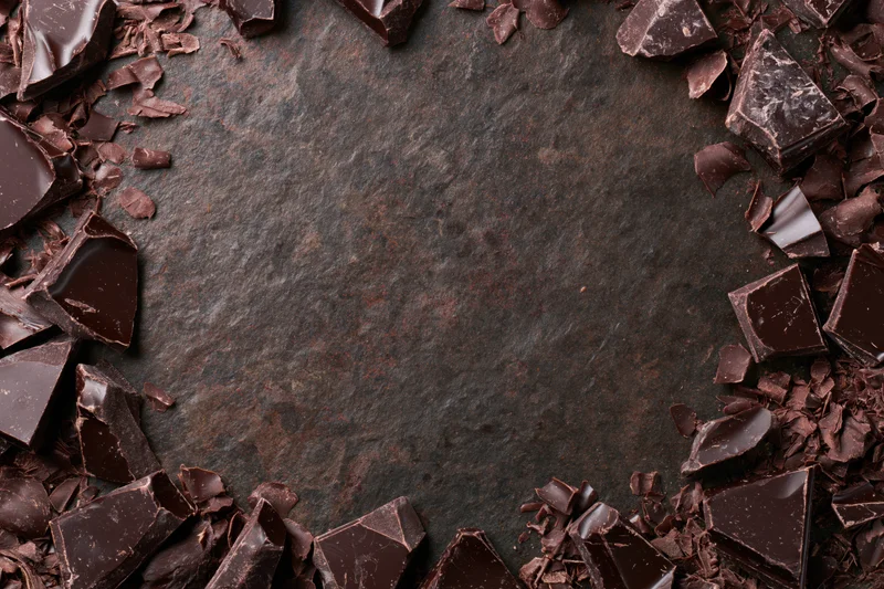 Broken dark chocolate chunks and shavings arranged in a frame around a dark stone surface