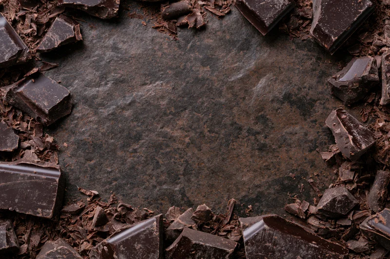Broken dark chocolate chunks and shavings arranged in a frame around a slate surface with copyspace in center