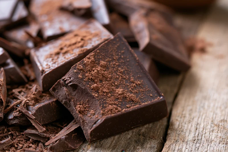 Broken dark chocolate pieces scattered on a rustic wooden surface