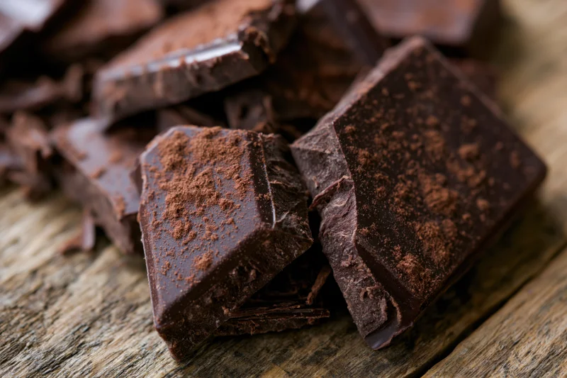 Broken dark chocolate pieces scattered on a rustic wooden surface