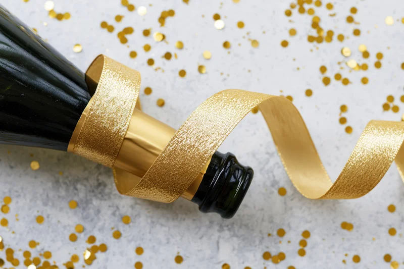 Champagne bottle lying on its side with a curled gold ribbon on a surface scattered with gold confetti