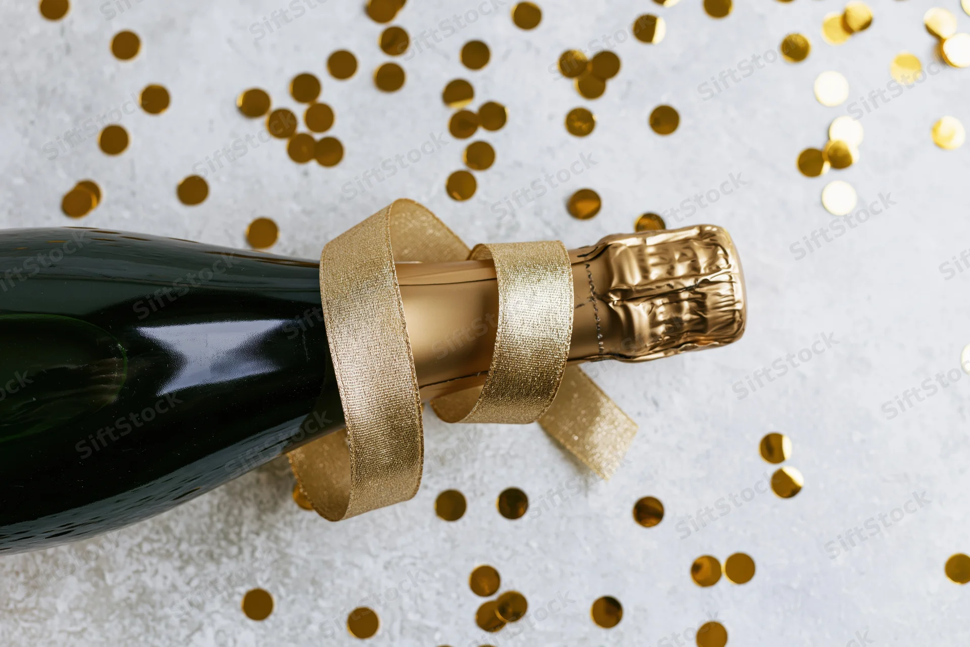 Champagne bottle with gold ribbon lying on white surface surrounded by confetti