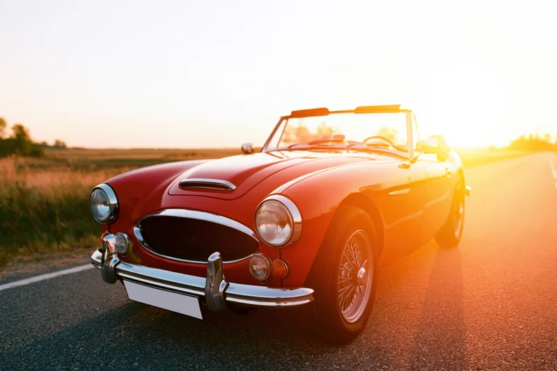 Classic red convertible sports car parked on rural road at sunset