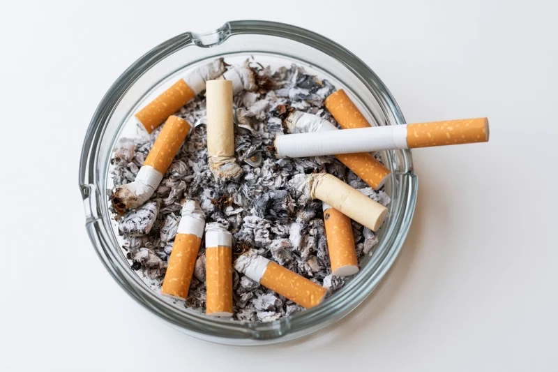 Clear glass ashtray filled with cigarette butts and ash on white surface