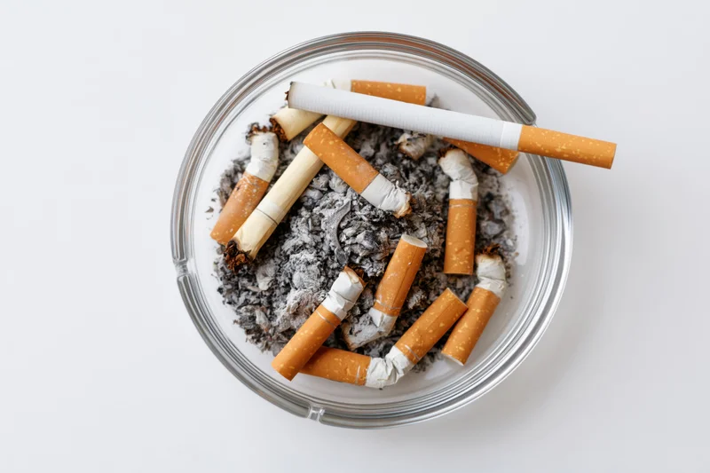 Clear glass ashtray filled with cigarette butts and ash on white background