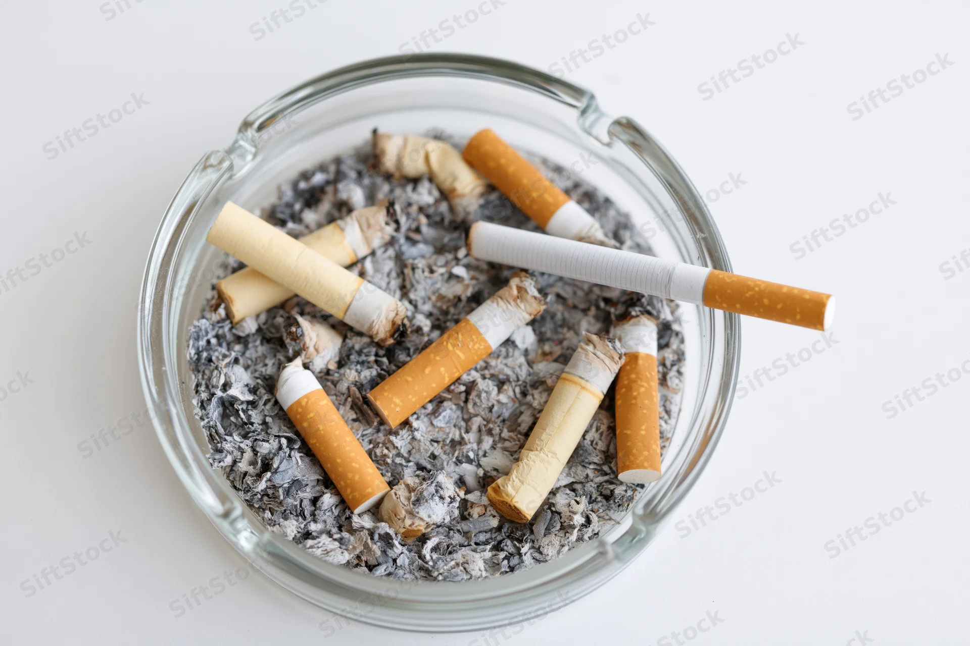 Clear glass ashtray filled with stubbed-out cigarettes and ash on white surface