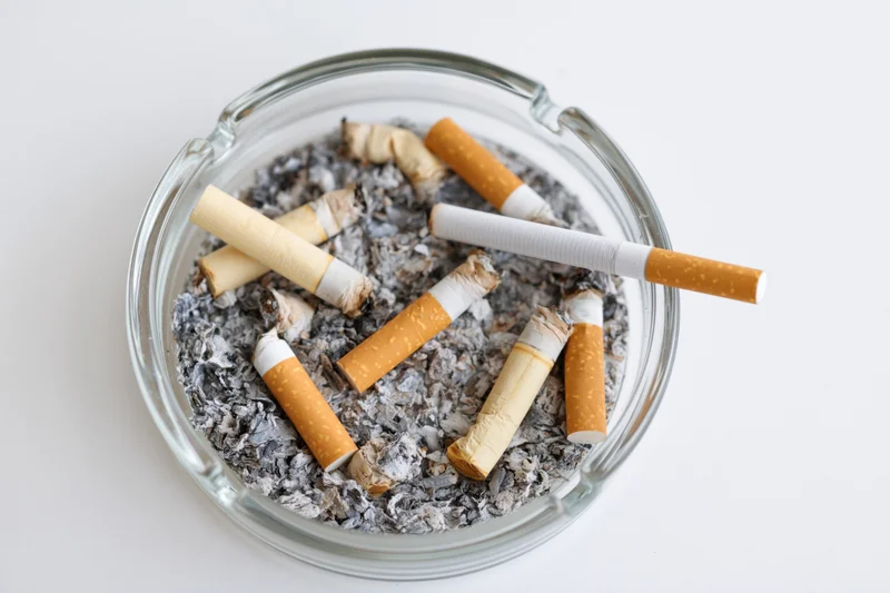 Clear glass ashtray filled with stubbed-out cigarettes and ash on white surface