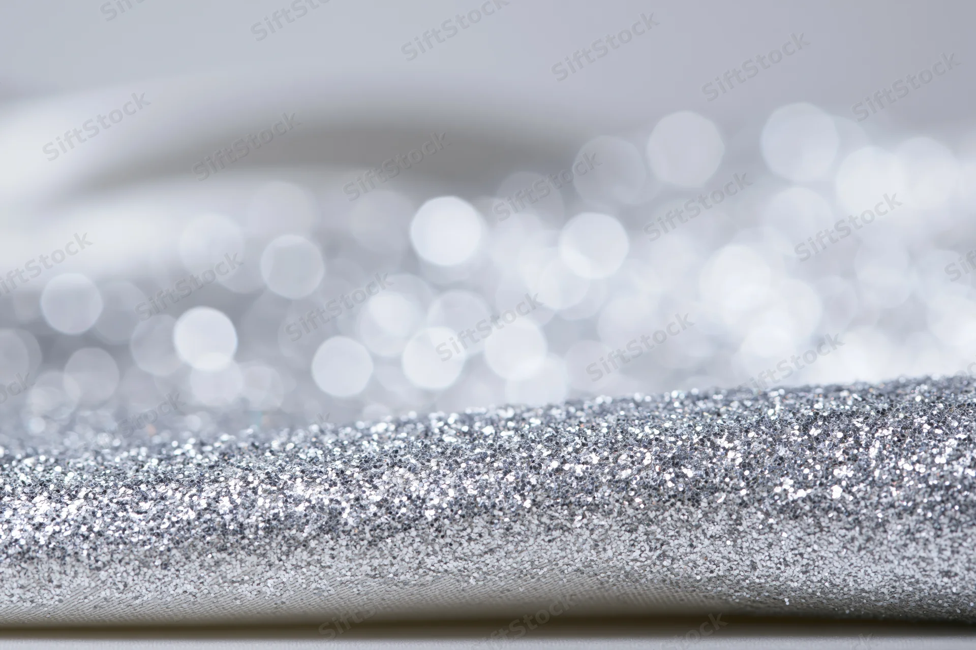 Close-up of silver glitter fabric with bokeh light effect in background