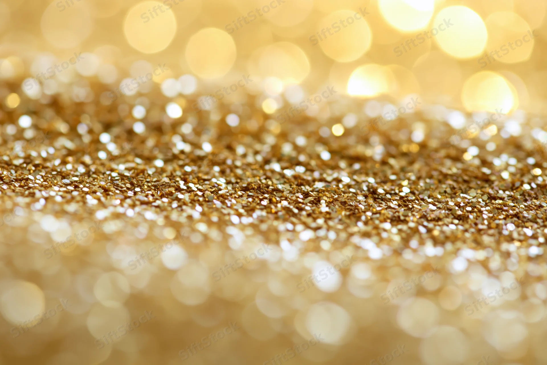 Close-up of scattered gold glitter particles with bokeh lights in the background