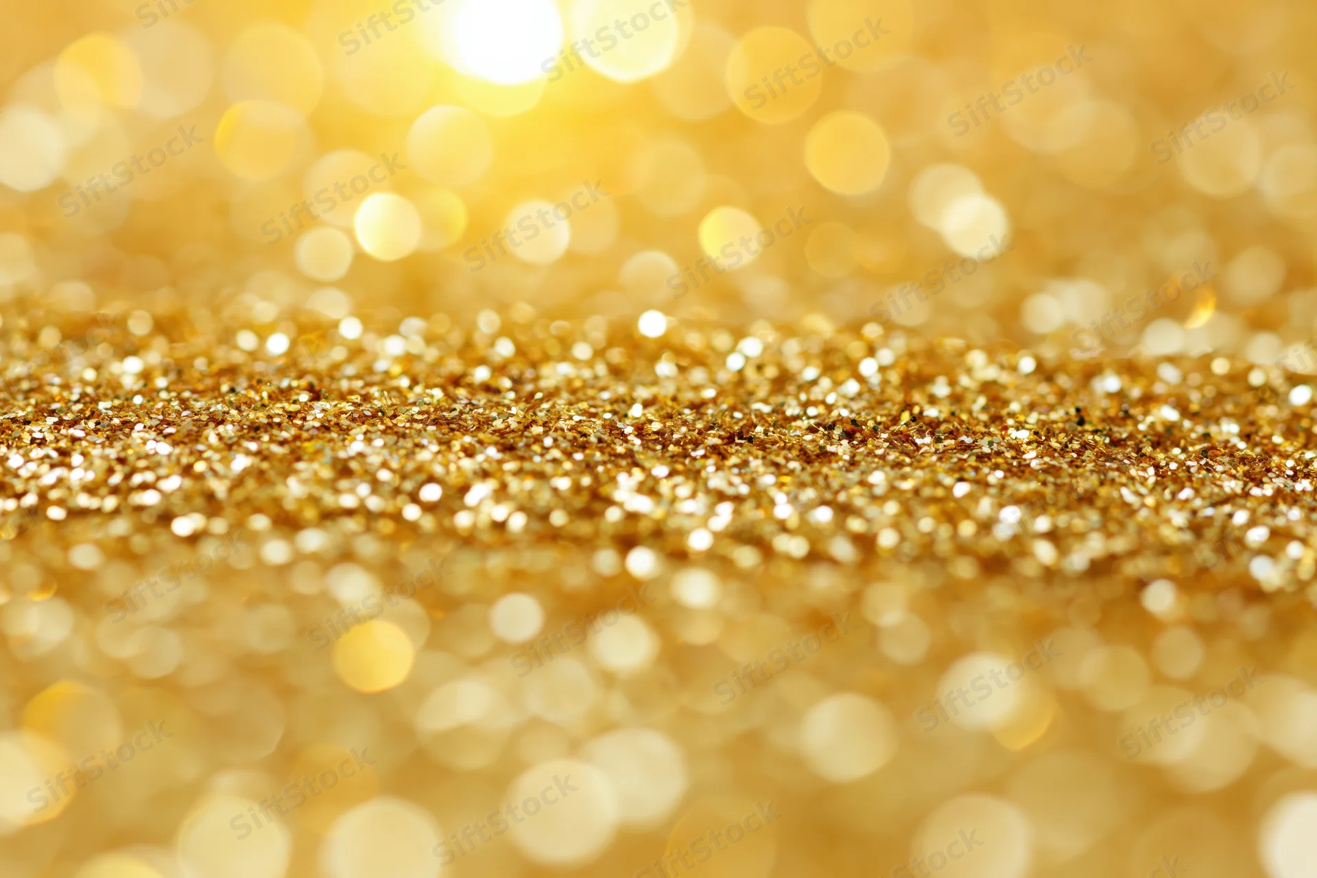 Close-up of scattered gold glitter particles with bokeh lights in the background