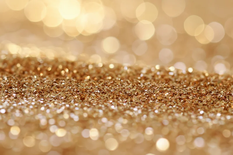 Close-up of scattered gold glitter particles with bokeh lights in the background