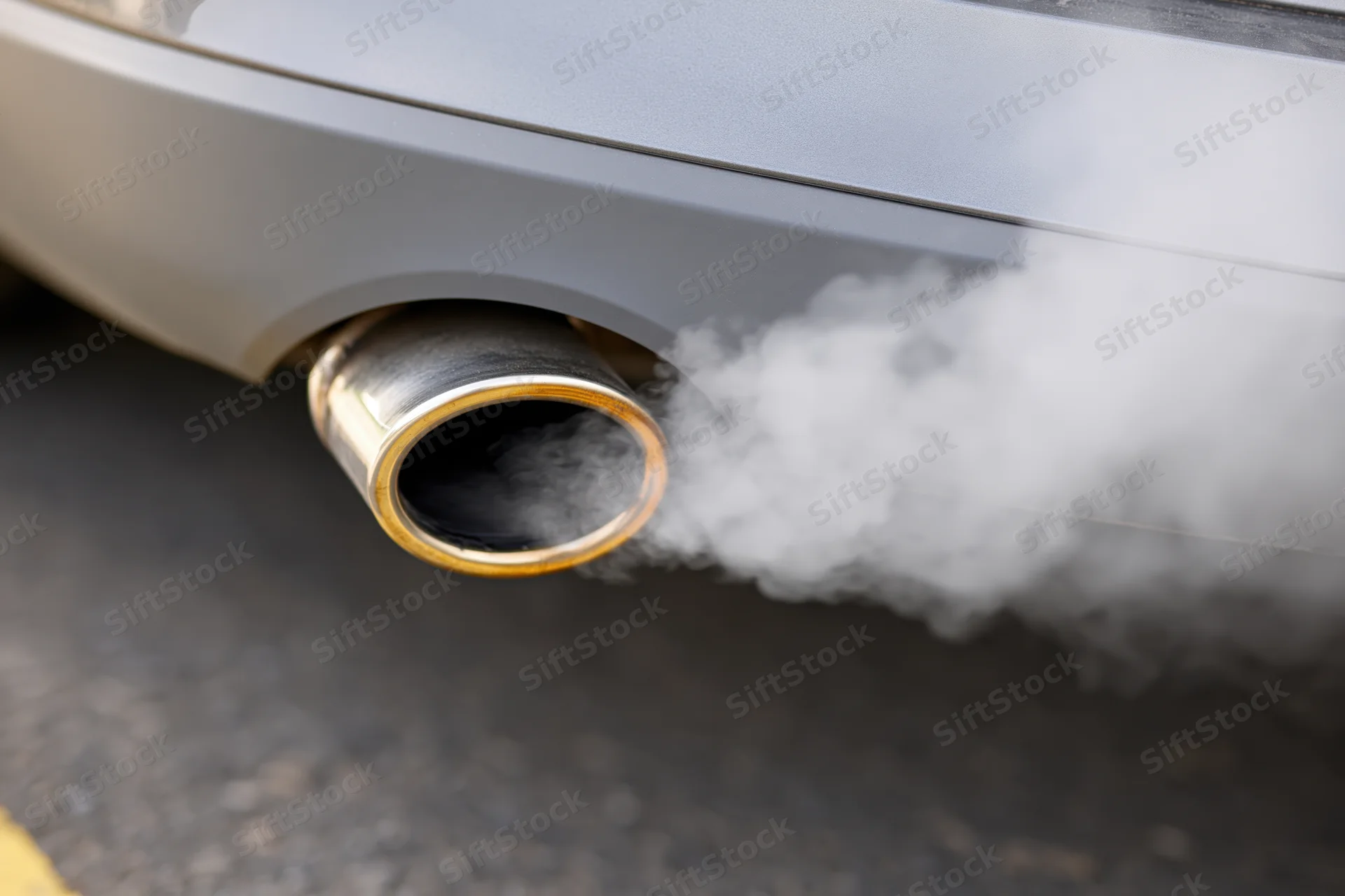 Close-up of car exhaust pipe emitting thick white smoke on asphalt road