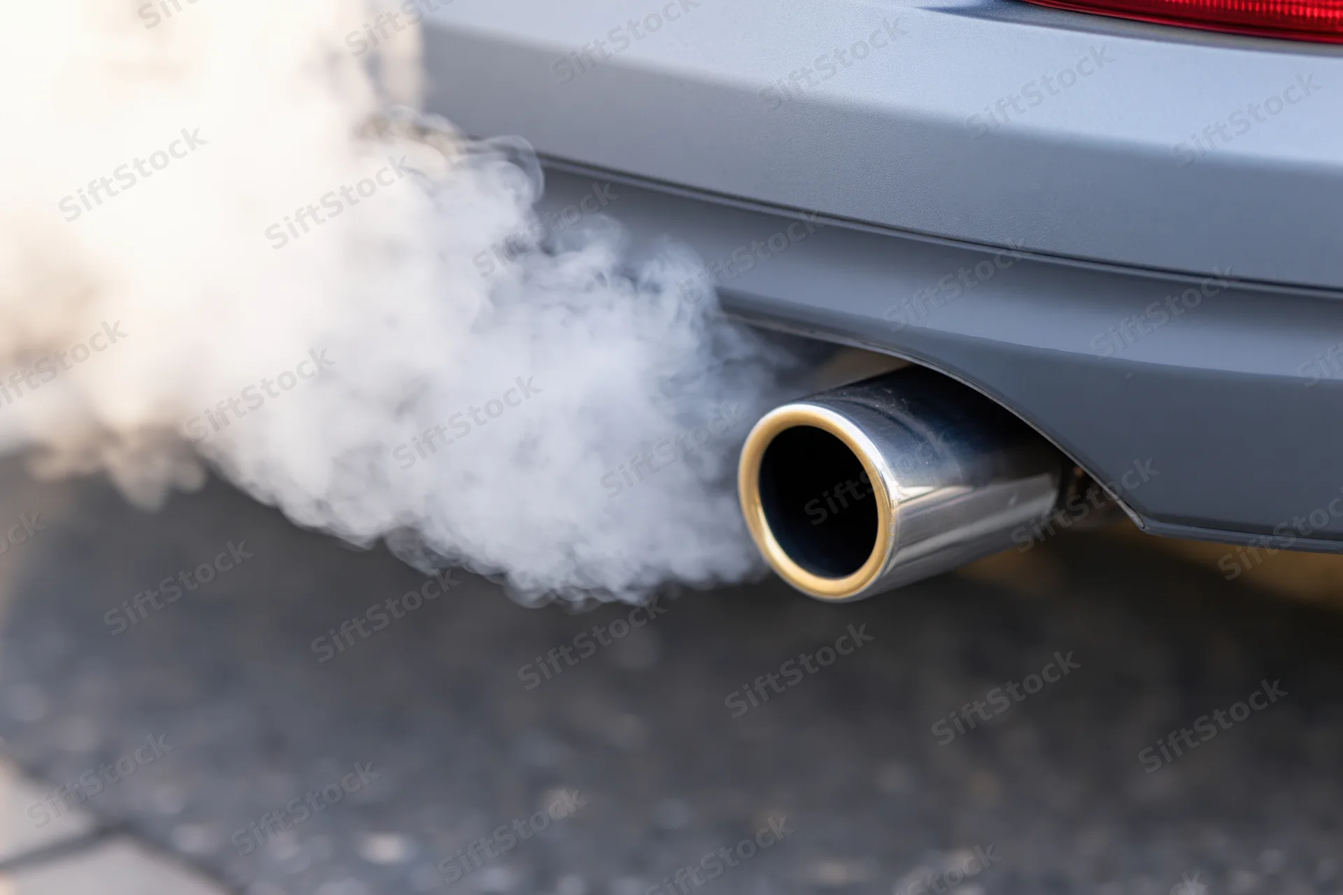 Close-up of car exhaust pipe emitting thick white smoke on asphalt road