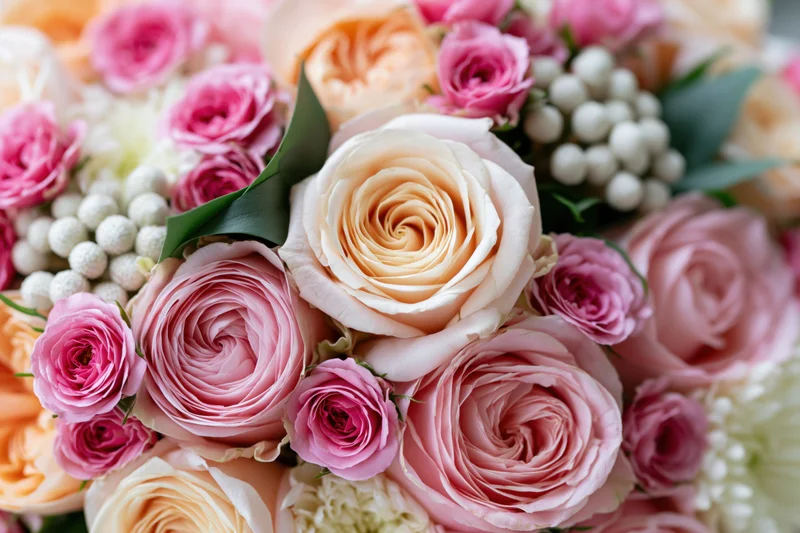 Close-up of a dense floral arrangement of pink and peach garden roses with white berries and green leaves