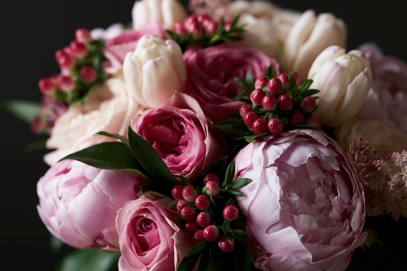Close-up of a lush floral bouquet with pink peonies, roses, tulips and berries arranged with greenery