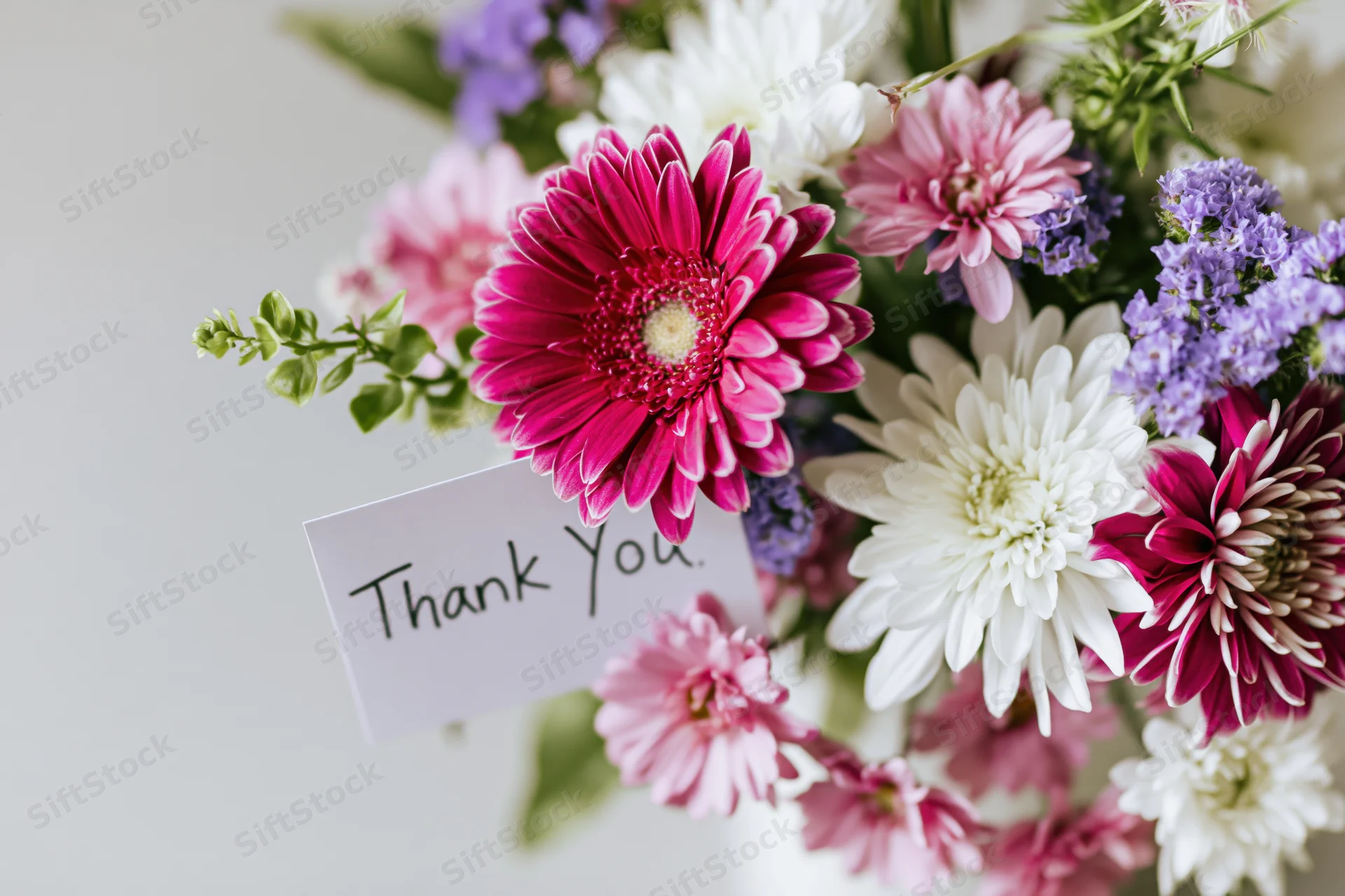 Close-up of a mixed flower bouquet with a handwritten thank you card attached to the stem