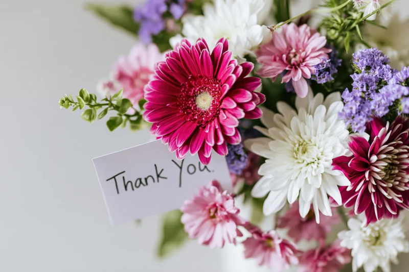 Close-up of a mixed flower bouquet with a handwritten thank you card attached to the stem