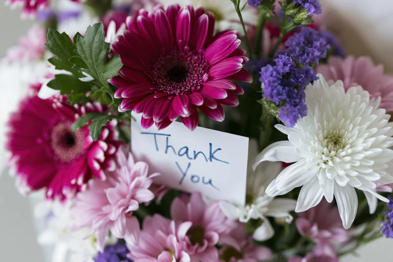 Close-up of a mixed flower bouquet with a handwritten thank you note tucked among the blooms