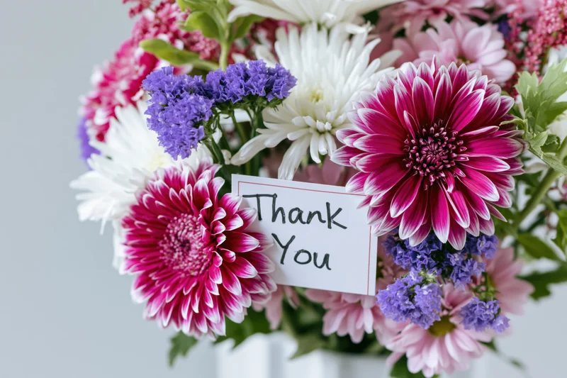 Mixed flower bouquet with thank you card inserted among blooms in white vase