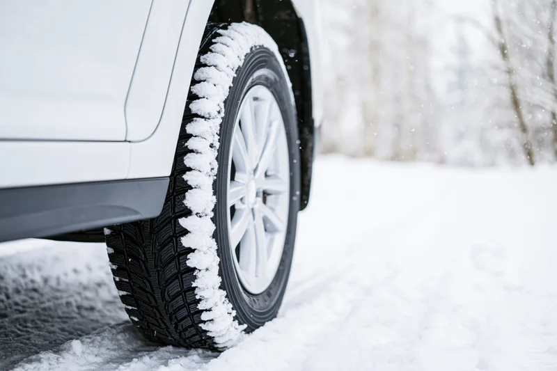 Close-up of a white car's rear winter tire on a snow-covered road