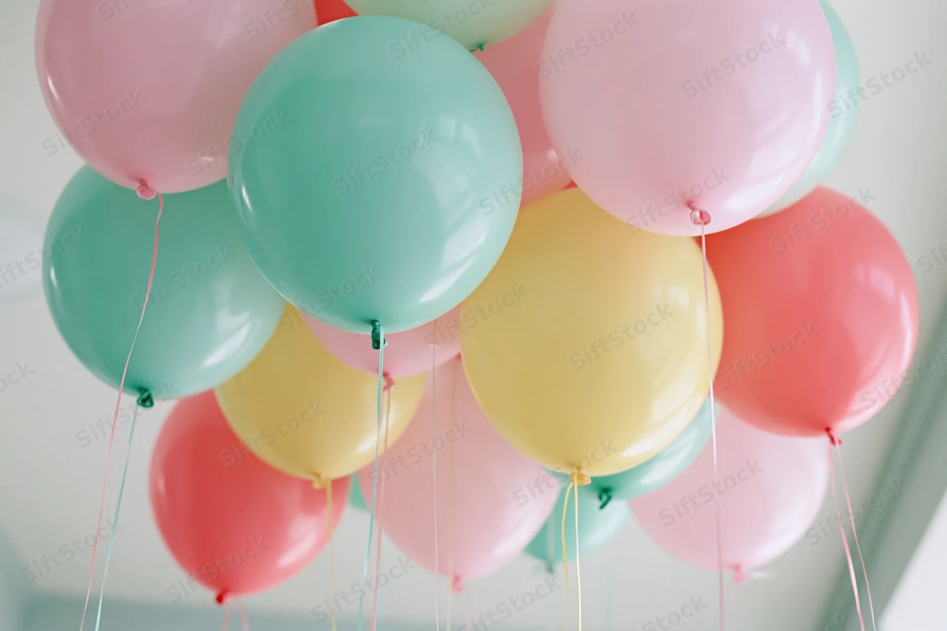 Cluster of pastel-colored helium balloons floating indoors against a white ceiling