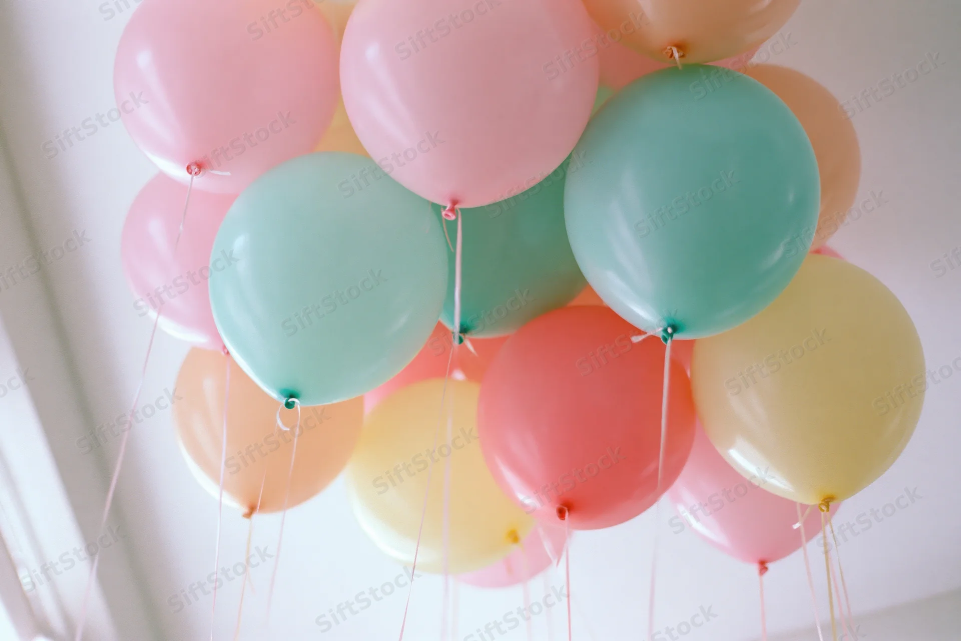 Cluster of pastel-colored helium balloons floating against a white ceiling indoors