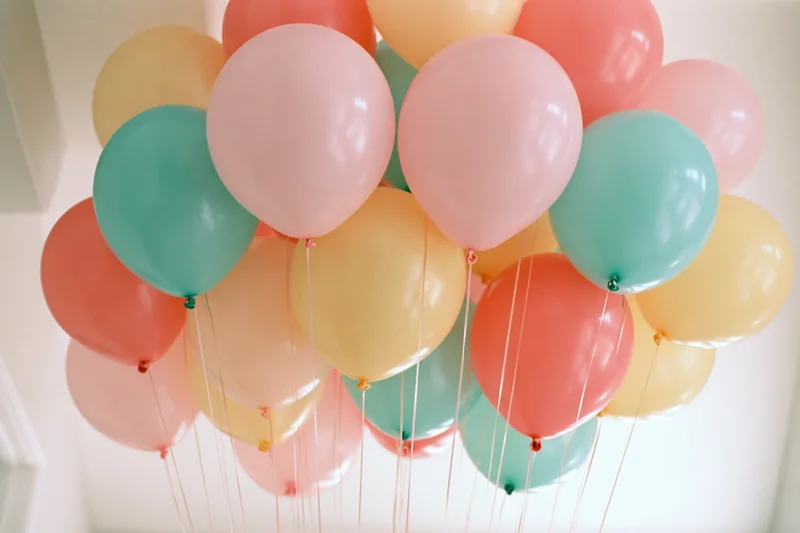 Cluster of helium balloons in pastel colors floating indoors against a white ceiling