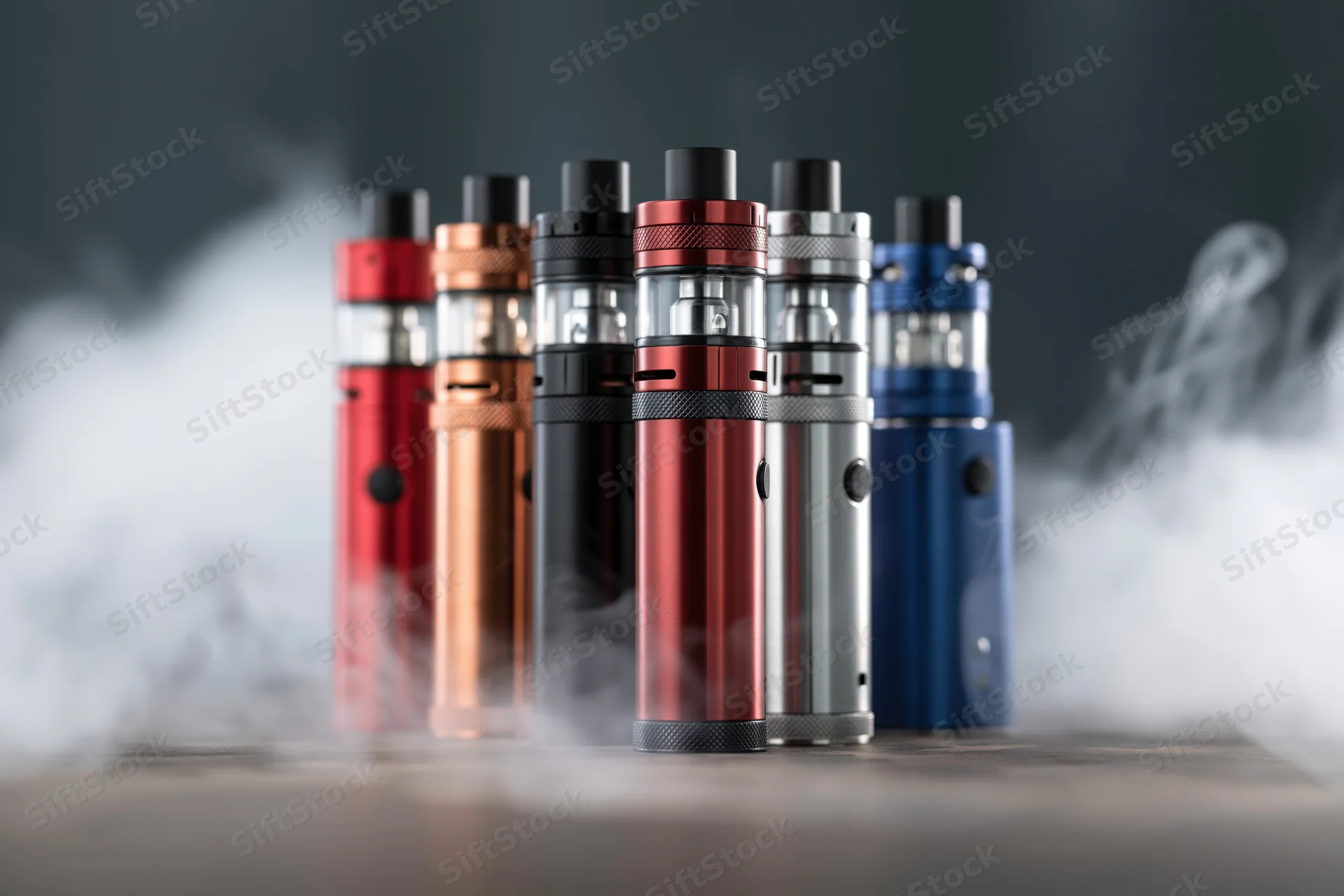 Collection of vape mods and tank atomizers arranged upright on a dark surface with vapor swirling around them