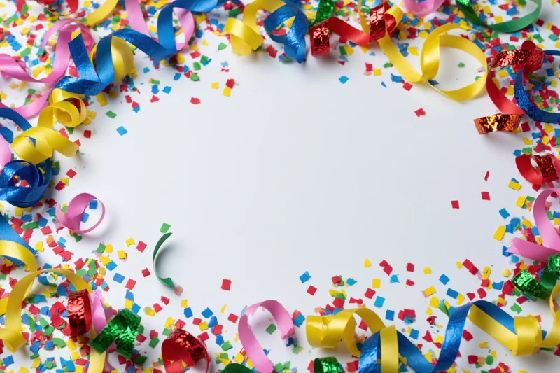 Colorful paper confetti and curled ribbon streamers scattered around white background forming a festive border with copyspace in center