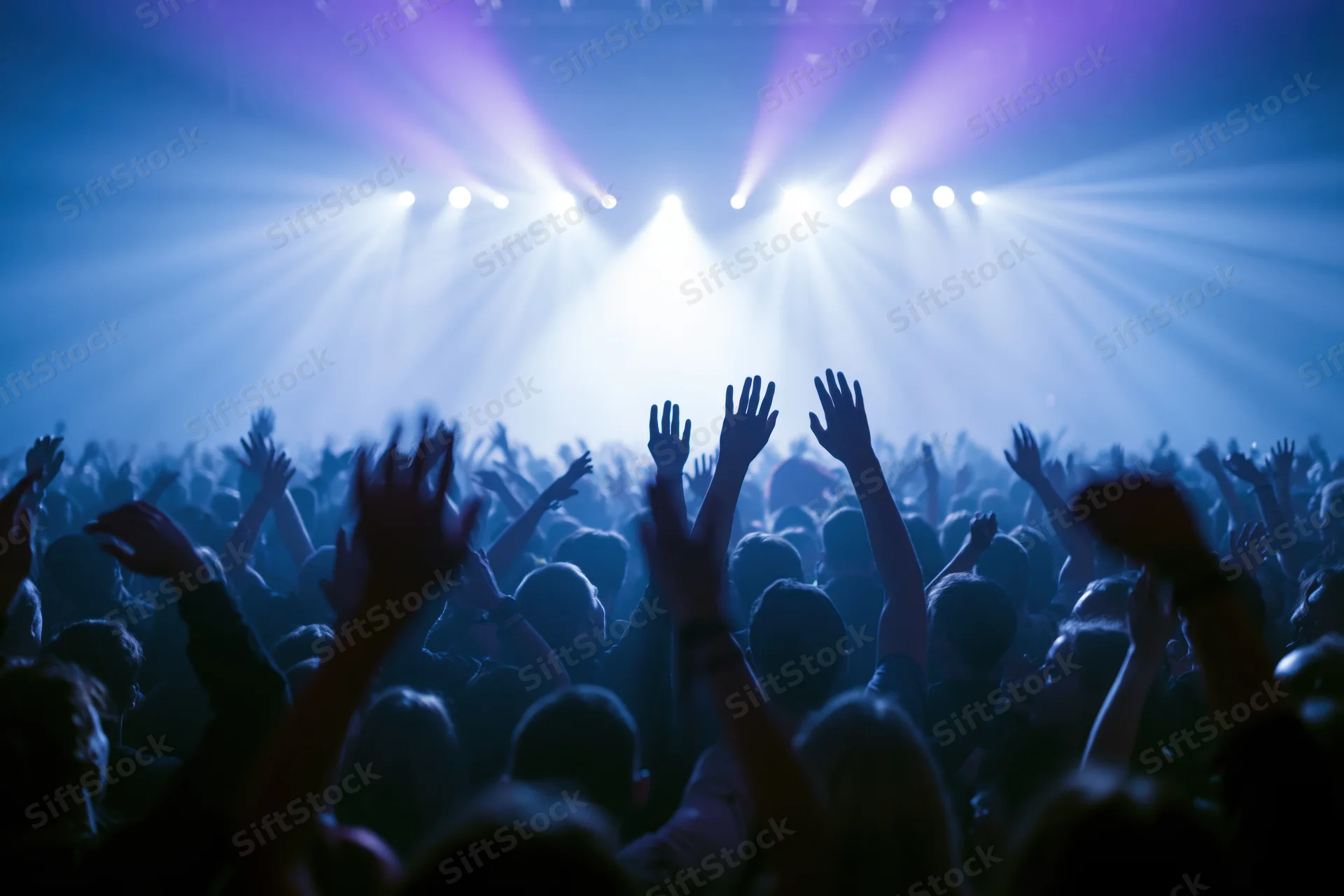 Crowd with hands raised toward bright stage lights at concert