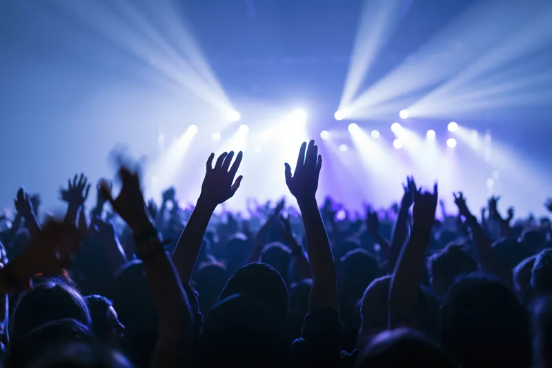 Crowd with hands raised toward bright stage lights at concert