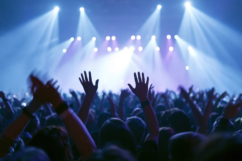 Crowd with hands raised toward bright stage lights at concert