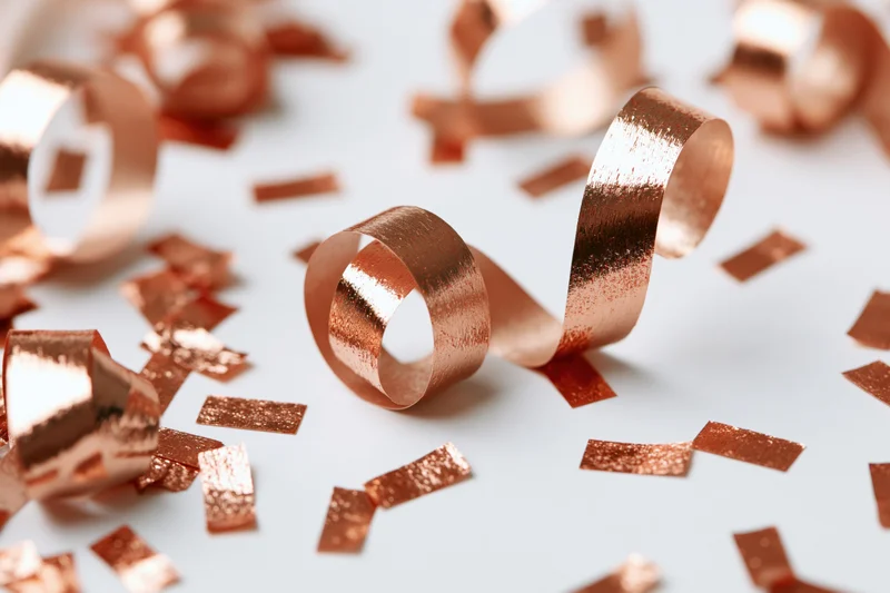Copper metallic streamers and confetti pieces falling mid-air on a white surface