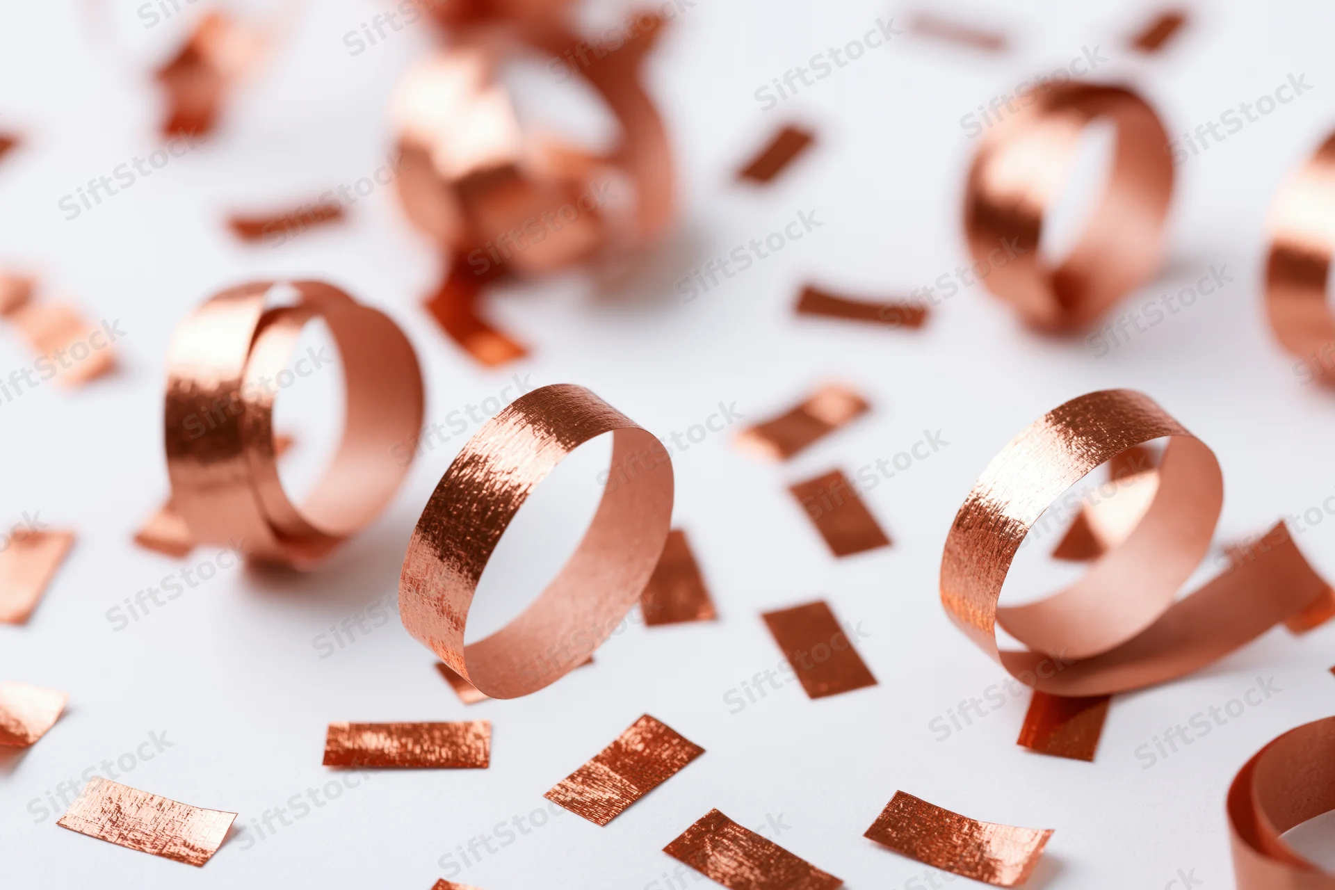 Copper metallic streamers and confetti pieces scattered on white surface
