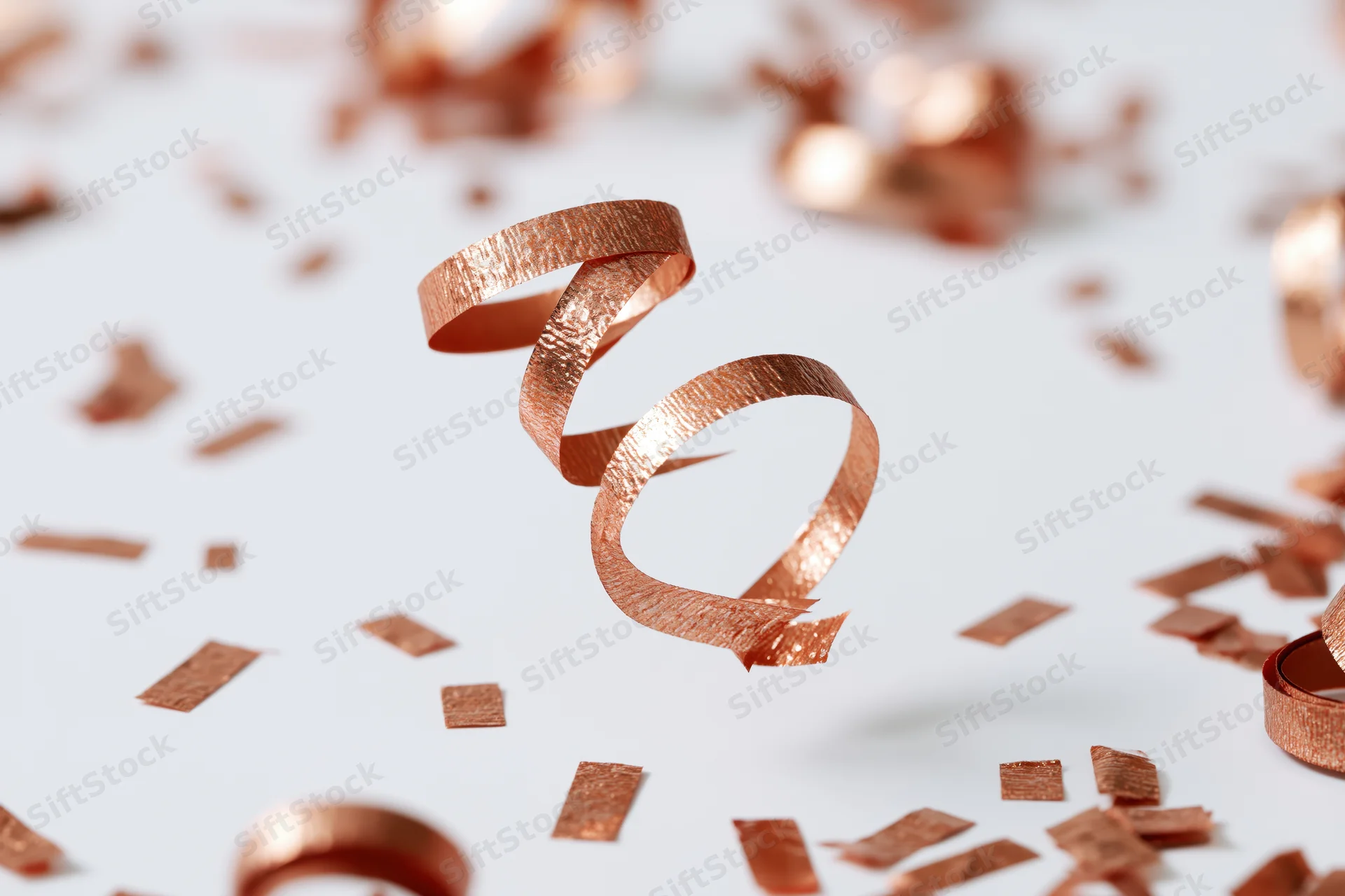 Copper metallic streamers and confetti pieces falling mid-air against a white background